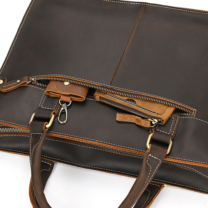 Dark brown briefcase with the top zip open, showing an inside zip pocket and a key clip